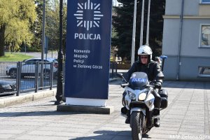 zdjęcie kolorowe, policjant w białym kasku motocyklowym siedzący na policyjnym motocyklu obok granatowego pylonu z napisem Komenda Miejska Policji w Zielonej Górze