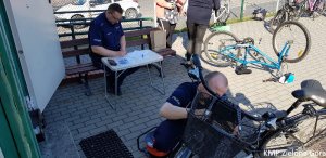 fotografia kolorowa, policjant znakuje rower i policjant wypełniający dokumentację