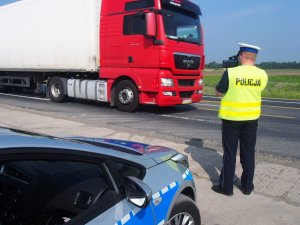 fotografia kolorowa, policjant z fotoradarem, w tle samochód ciężarowy