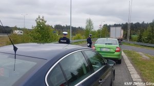 Zdjęcie kolorowe. Policjanci ruchu drogowego zatrzymali do kontroli drogowej kierującego zieloną skodą rapid.