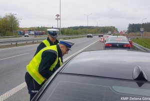 Zdjęcie kolorowe. Policjanci ruchu drogowego stoją przy kontrolowanym samochodzie BMW i rozmawiają z kierującym.