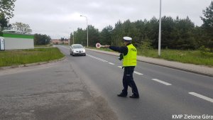 Zdjęcie kolorowe. Policjant ruchu drogowego zatrzymuje do kontroli samochód marki seat.