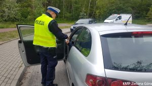 Zdjęcie kolorowe. Policjant ruchu drogowego stoi przy samochodzie marki seat i bierze dokumenty od kierującego.