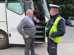 Policjant sprawdzający alkomatem kierowce autobusu z zamazaną twarzą