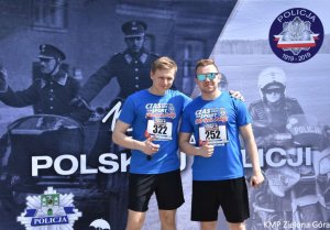 Dwóch mężczyzn stojących na tle plakatu biegu z okazji 100-lecia Polskiej Policji