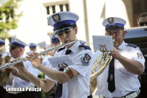 Policjantka grająca na flecie poprzecznym a w tle orkiestra policyjna