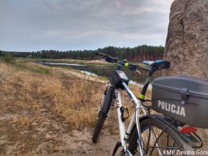 Zdjęcie roweru policyjnego opartego o głaz nad stawem