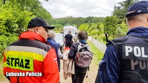 Zdjęcie policjantów prowadzących dwie kobiety przez ogródki działkowe