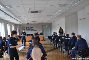 Zdjęcie policjantów siedzących w ławkach szkolnych oraz policjanta rozdająca kartki