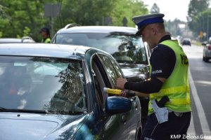 Zdjęcie policjanta sprawdzającego alkomatem trzeźwość kierowcy siedzącego w aucie