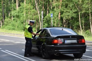 Zdjęcie policjanta sprawdzającego alkomatem trzeźwość kierowcy siedzącego w czarnym aucie