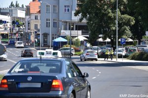 Zdjęcie zrobione z ulicy na dwie policjantki stojące przy radiowozie oraz na ruch drogowy