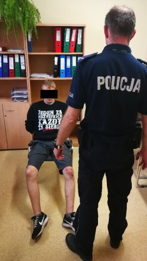 Policjant stoi przed siedzącym zatrzymanym