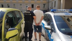 Policjant prowadzi zatrzymanego do wozu policyjnego