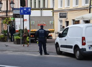 Jeden policjant rozmawia z kierowcą nieprawidłowo zaparkowanego samochodu dostawczego a drugi policjant czeka na kierowce drugiego nieprawidłowo zaparkowanego samochodu