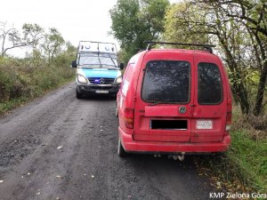 Na szutrowej drodze stoi radiowóz Policji oraz czerwone małe autko dostawcze