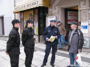 Policjant z młodzieżą rozdający ulotki seniorowi