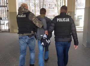 Aresztowany mężczyzna prowadzony przez policjantów.