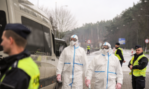 Policjanci w specjalnych kombinezonach sprawdzający temperaturę ciała osób wjeżdżających na teren RP.