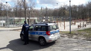 Policjant z radiowozem na tle boiska oraz placu zabaw