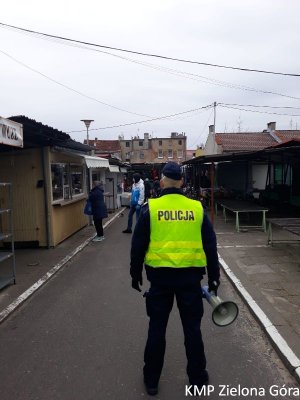 Policjant w mundurze, odblaskowej kamizelce z megafonem na targowisku