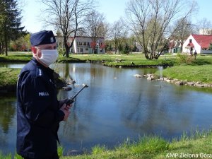 Policjant w maseczce ochronnej patroluje okolice stawu.