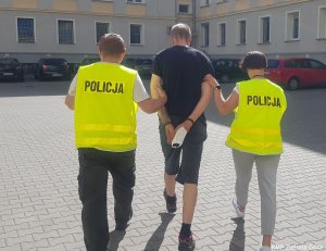 zatrzymany mężczyzna prowadzony przez policjantów.