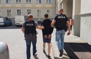 Policjanci na dziedzińcu Komendy Miejskiej Policji w Zielonej Górze prowadzą poszukiwanego.