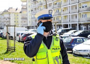 Policjant z maską i w rękawiczkach rozmawiający przez telefon komórkowy.