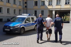 Aresztowany mężczyzna zakuty kajdankami prowadzony przez policjantów do radiowozu