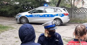 Policjantka ruchu drogowego rozmawia z dziećmi, w tle policyjny radiowóz