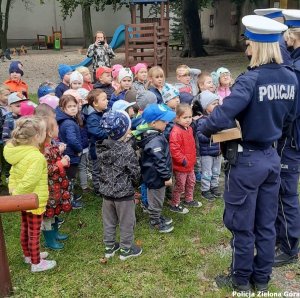 Policjanci ruchu drogowego rozmawiają z dużą grupą z dzieci, w tle plac zabaw