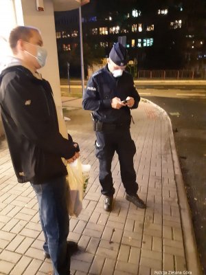 Policjant w masce legitymuje obywatela przed sklepem