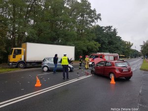 Na środku drogi stoją dwa osobowe samochody i jedna ciężarówka, jest też Policjant i Straż Pożarna