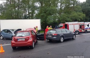 Sytuacja po zdarzeniu drogowym - na środku drogi stoją trzy samochody, jedna ciężarówka oraz służby medyczne i gaśnicze