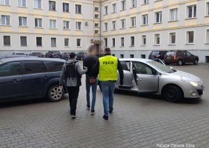 Policjanci prowadzą zatrzymanego który ma założone kajdanki na rękach