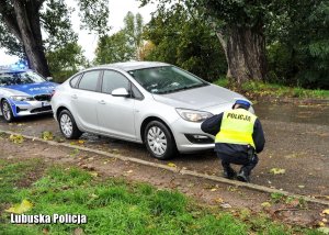 Policjant kuca przy srebrnym samochodzie