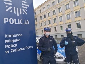 Policjanci stoją na tle Komendy i radiowozu