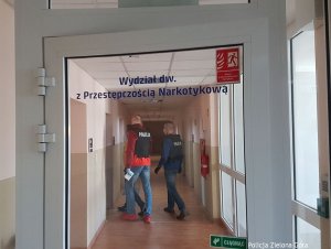 Zdjęcie przedstawia drzwi do Wydziału do walki z Przestępczością narkotykową a za nimi dwóch policjantów