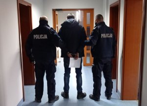 Policjanci trzymają zatrzymanego w budynku Komendy