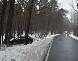Droga podczas zimy - na poboczu stoi zaparkowany radiowóz policyjny a obok uszkodzony czarny pojazd