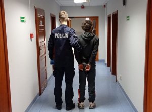 Policjant trzyma zatrzymanego w budynku Komendy