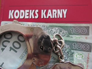 Na książce Kodeks Karny leżą banknoty 100zł oraz kajdanki