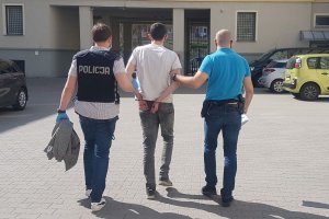 Dwóch nieumundurowanych policjantów prowadzi zatrzymanego na dziedzińcu Komendy