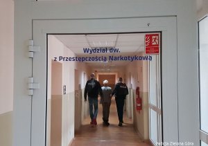 Dwóch funkcjonariuszy prowadzących mężczyznę przez korytarz