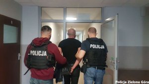 Dwóch uzbrojonych policjantów prowadzi mężczyznę w czarnej koszulce