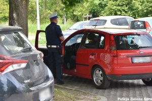 Policjant rozmawiający z kierowcą czerwonego samochodu