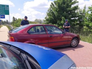 Policjanci legitymujacy kierowce zatrzymanego czerwonego  samochodu