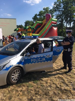 Dwóch policjantów patrzy na dzieci wsiadające do radiowozu.