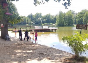 Dwóch funkcjonariuszy stoją na plaży i rozmawiają z wypoczywającymi ludźmi